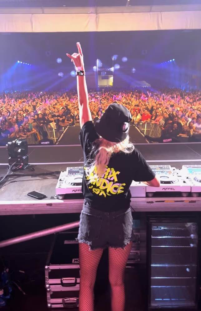 CANDICE unosi rękę nad konsoletą DJ-ską w stronę publiczności